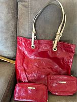 Photo of the red Michael Kors tote bag showing embossed logo pattern and beige adjustable handles.