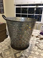 Large galvanized metal olive bucket on lace tablecloth showing size and shape with handles.