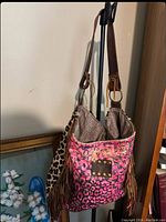 View of the full bag showcasing multicolor leopard print, fringe sides, and shoulder strap.
