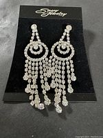Photo shows a pair of Sassy South dressy formal earrings with clear rhinestones arranged in circular patterns and long dangling fringe.