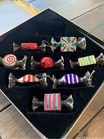 Photo of 8 Thomas Paccon Museum Series candy-shaped Christmas ornaments arranged in a black box with compartments.