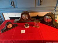 Full display of five clocks including three wooden mantel clocks and two smaller clocks on a red tablecloth