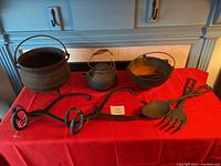 Full view of all items on red cloth including the teapot, stove bowls, oversized fork and spoon utensils, and small skillet