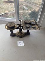 Antique Fairbanks cast iron balance scale with brass weights on the weighing platform and display of the scale on a table near window.