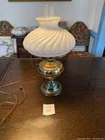 Full view of the brass hurricane lamp with milk glass dome and attached clear chimney on a wooden table.