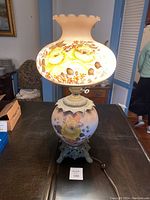 Front view of the lamp fully assembled on a table, showing the painted yellow roses on the frosted glass shade and base.