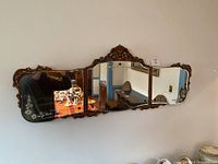 Full front view of long antique gilded wall mirror with three glass panes and intricate carved frame hanging on wall.