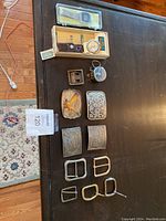 Overview photo showing the watches, pocket watch, and belt buckles laid out on a dark table surface.