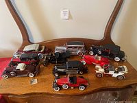Top-down view of 10 model cars arrayed on wooden table showing various colors and roof styles