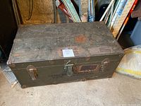 Front view of closed trunk showing locking latch, leather handle and stencil text