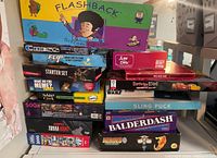 Stack of boxed board games and puzzles including Flashback Sitcom Edition, Chess Flip Starter Set, Poker, Cards Against Star Wars, Sling Puck and Balderdash.