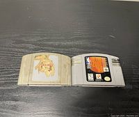 Photo showing two Nintendo 64 cartridges side by side on black surface, the right cartridge is NBA In The Zone '98 and left cartridge label is torn off.