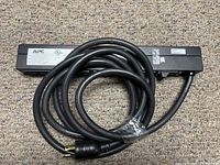 View of the power strip laid flat showing the APC power strip with attached power cable coiled on top.