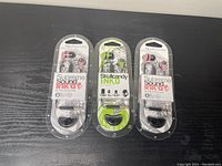 Three new sealed Skullcandy Ink'd headphones in original blister packaging placed side by side on a black surface.