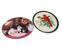 Two oval decorative plates, one with cats and flowers, the other with cardinals and foliage, showing color, design, and condition.