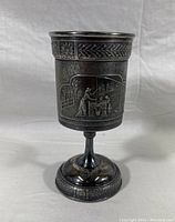 Front view of the chalice showing detailed embossed relief of adult and children pulling water from a well, ornate rim and base detailing, aged patina and imperfections.