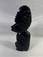 Side view of glossy black obsidian statuette showing detailed Mayan or Aztec inspired carving including headdress and facial features.
