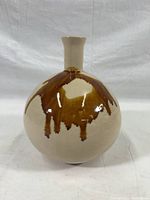 Front angled view of beige pottery vase with brown drip glaze, showing round body and narrow neck
