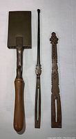 Photo showing the antique goffering iron with wooden handle alongside two long metal tweezer clamp style tools on a white background.