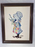 Full view of the framed Holly Hobbie needlepoint embroidery artwork showing the entire piece within a dark wood frame with a gold inner trim.