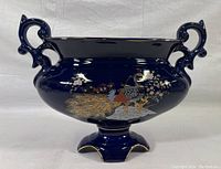 Front side angle view of cobalt blue hand painted porcelain dish with two handles and peacock design.