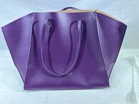 Full view of purple leather handbag with double straps and gold foil Serena Williams logo on front.