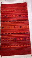 Full view of the rectangular woven rug dominated by red and orange colors with geometric patterns and stripe bands.