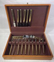 Open wooden box revealing 6 cutting knives in the upper section and spoons and forks in the lower section, all with polished stainless steel handles.