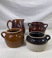 Front view of set showing all four pieces: large dark brown pitcher and three pottery pots in varying brown and tan glazes