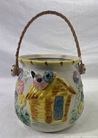 Front view of ceramic jar showing 3D bird and house design with handle and no lid.