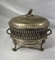Front angle of vintage silver-plated chafing dish showing detailed lid with decorative knob, pierced mesh side panel, and ornate curved feet.
