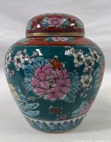 Front view of ginger jar showing pink peony and cherry blossom floral motifs on turquoise background with rust-colored top lid.