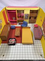 Full top-down view of the vintage Barbie Dream House interior showing the cardboard walls and floor with furniture pieces arranged inside including sofa, chairs, dresser, and coffee table.