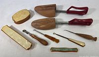 Photo showing two wooden shoe stays with red handles and various shoehorns and button hooks of Bakelite and wood with mother-of-pearl inlays.
