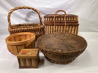 Photo of five vintage woven baskets and wooden box arranged on white background showing variety of shapes, weaves, and materials.