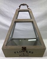 Full view of trapezoidal wood and glass terrarium showing front, glass panels, metal latch, and top handle