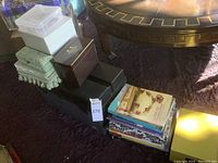 Wide view of black toolbox on purple rug, stacked with multiple boxes and books at its base.
