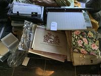 paper cutter, stacked plastic storage boxes, papers and fabric fabrics with floral and crane embroidery