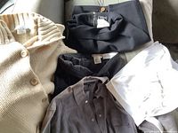 Cream knit cardigan, black trousers, gray top and white blouse arranged on couch