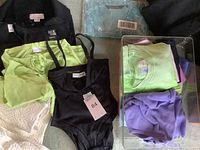 Overview showing black sweater, green cashmere sweater, black bodysuit, and assorted tees in a container.
