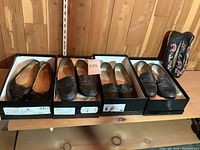 Overview of four pairs of Chanel flats in boxes on wooden shelf.