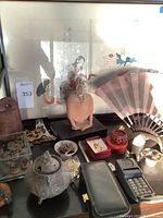 Overview of Asian print background, terracotta head sculpture, red lacquer jar, folding fan, earrings, incense burner and assorted items