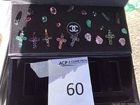 Tray view showing five crucifix pendants, loose faceted gemstones, carved stone beads on black background