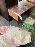 Open drawer containing multiple folded loungewear pieces in garment bags and loose pants on floor