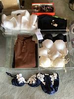 Overhead view of four clear storage containers showing white sweater, brown knit pullover, black DKNY top, cardboard box of belts