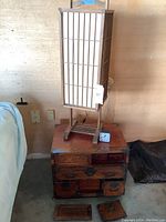Wooden table with drawers, Asian style tall lamp with stained paper panels, small analog clock, and vintage corded phone on top