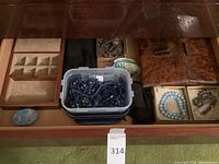Drawer with multiple compartments showing tray, plastic bead container, abalone shell, wood and gold-tone boxes