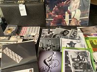 Overview showing black ostrich briefcase on left, assorted stamps and a selection of printed celebrity photos including boxing match and headshots.