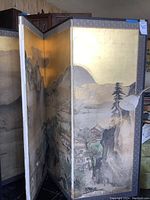 View of first folding room divider showing mountainous landscape scene with gold background, cardboard edges, and signs of wear.