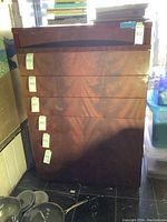 Front view of six-drawer wooden lacquered dresser with tags on each drawer